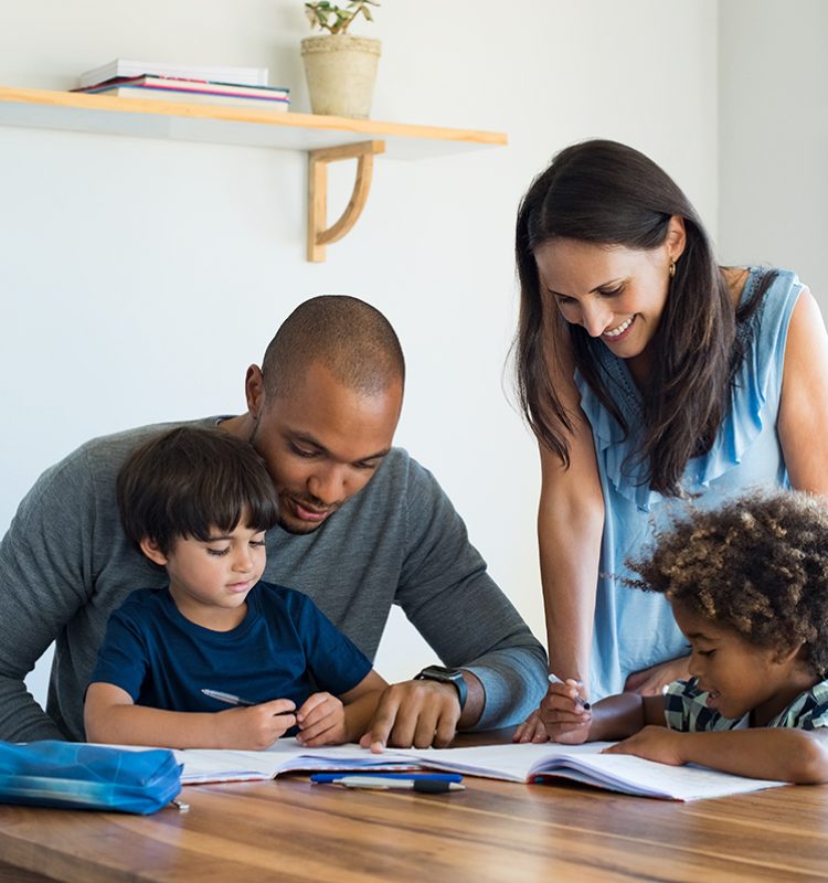 Multiethnic parents helping children with their homework at home. Young father and mother helping sons study at living room. Little boys completing their exercises with the help of dad and mom.